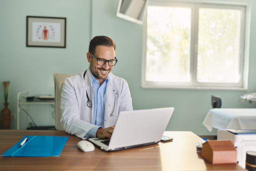 Happy male doctor working on laptop in the office.